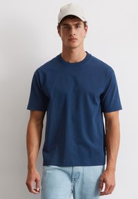 Granatowa bawełniana koszulka z okrągłym dekoltem i krótkimi rękawami, noszona z jasnoniebieskimi dżinsami. Prosty design, bez widocznych wzorów czy akcentów.
