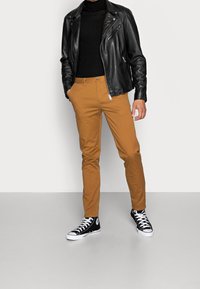 Černá kožená moto bunda, černý rolák, pískové úzké chino kalhoty a černé vysoké tenisky s bílými podrážkami. Texturované materiály.