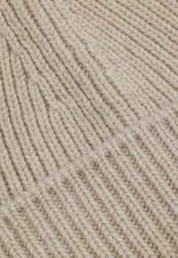 Jasnobeżowa dzianina o prążkowanej fakturze, z wyraźnymi ukośnymi liniami i miękkim, grubym wyglądem. Bez widocznych wzorów ani ozdób.