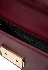 Interno di una borsa in pelle marrone con una chiusura a molla in metallo dorato e una tasca con zip nera con logo ripetuto. Texture liscia.