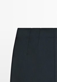 Pantaloni neri a vita alta con parte anteriore liscia, cuciture verticali e tessuto dalla texture liscia. Presentano sottili dettagli di cucitura lungo la vita.