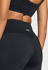 Μαύροι ψηλόμεσοι κολάν κατασκευασμένοι από ελαστικό ύφασμα, με ομαλή υφή και ραμμένες λεπτομέρειες. Το λογότυπο βρίσκεται στη μέση της ζώνης.