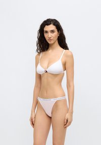 Σετ μπικίνι από λευκό ύφασμα με τριγωνικό σουτιέν που διαθέτει λεπτές τιράντες και ένα διακοσμητικό στο κέντρο. Το κάτω μέρος έχει λάστιχο με λογότυπο σε ανοιχτό ροζ και μπλε χρώμα.