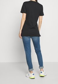 Svart bomullströja med rund halsringning, matchad med blå denimjeans. Vita sneakers med gula och blå detaljer. Enkelt mönster, avslappnad passform.