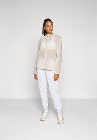 Transparent ljusbeige jacka med huva, dragkedja fram och subtil logotyp. Matchas med ljusgrå joggers och sneakers.