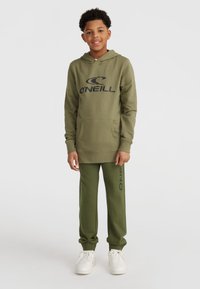 Olivgrüner Kapuzenpullover mit einer Vordertasche und schwarzem Logo, kombiniert mit passenden olivgrünen Hosen mit seitlichem Branding, getragen mit weißen Sneakern.