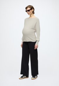 Béžový rebrovaný tehotenský top s voľnými rukávmi, kombinovaný s čiernymi nohavicami s širokými nohavicami a čierno-bielymi športovými topánkami. Nosené čierne slnečné okuliare.