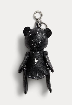 Breloc de urs din piele neagră texturată cu inele argintii și detalii cusute albe, având un mic logo alb cu jucător de polo pe piept.