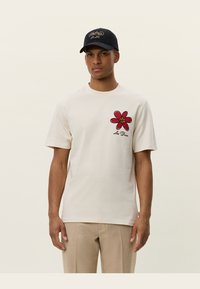 Camiseta corta de manga con un diseño de flor roja en el centro y un balón de baloncesto dentro, con el texto "Les Deux" debajo. Material de algodón suave.