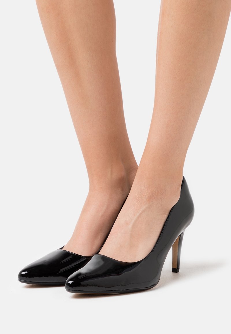Escarpins en cuir verni noir brillant avec une pointe effilée et un talon stiletto élancé. Texture lisse avec un design épuré et minimaliste.