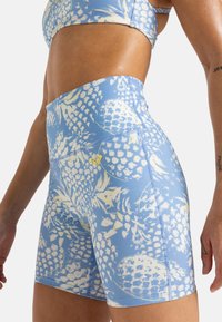 Shorts bleus taille haute en matière extensible avec un motif floral blanc, jaune et bleu, dotés de coutures contrastantes et d'un détail de logo.