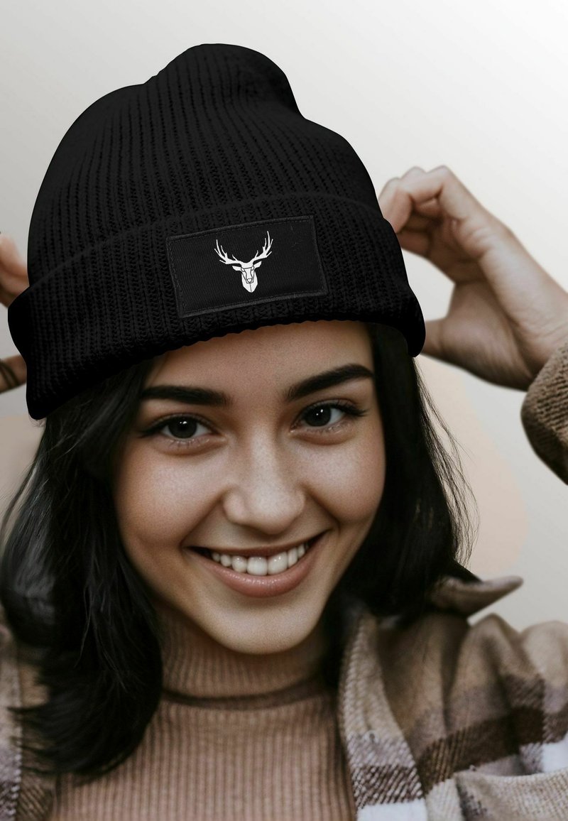 Black knitted beanie with a folded cuff, featuring a rectangular patch displaying a white deer graphic. Warm texture, fitted design.