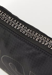 Black fabric bag featuring a textured pattern, silver hardware, and embossed logo detailing along the zipper area.