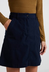 Navy blue cotton skirt with a fitted waistband, side pockets, and a straight cut. Features a front button closure and visible stitching details.