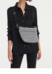 Borsa a tracolla grigia in nylon con una texture soffice, chiusura con zip e tracolla regolabile, indossata sopra una maglietta nera.