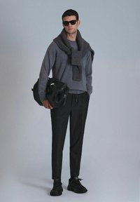 Grijze trui met een bijpassende sjaal, zwarte broek en sneakers. Het model houdt een zwarte tas vast, accessoires met een zonnebril.