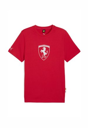Piros póló, amelyen a mellkason egy fehér Ferrari-logó, az ujjon pedig egy kis Puma-logó található, egyszerű fehér háttér előtt.