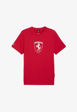 Piros póló, amelyen a mellkason egy fehér Ferrari-logó, az ujjon pedig egy kis Puma-logó található, egyszerű fehér háttér előtt.
