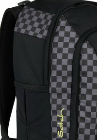 Sac à dos noir avec un motif en damier texturé noir et gris, poches latérales en filet et un logo jaune bien visible.