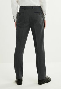 Pantalon à carreaux gris avec une coupe slim, doté de deux poches arrière et d'une texture lisse. Assorti à des chaussures de ville noires.