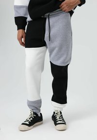 Color-blocked sweatpants featuring grey, black, and white panels. Made of soft material, with an elastic waistband and cuffed ankles.