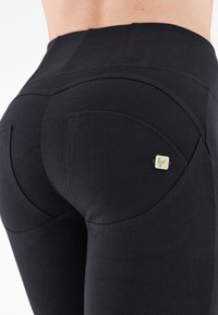 Leggings noirs avec une taille haute, présentant des coutures courbées, des surpiqûres doubles et un petit logo en accent sur la poche arrière.
