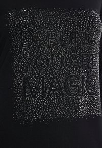 Schwarzes T-Shirt mit einem Design aus silbernen Strasssteinen, das "DARLING YOU ARE MAGIC" buchstabiert, strukturiert mit verschiedenen Größen und Mustern von Steinen.