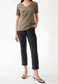 Oliwkowa koszulka z dekoltem w serek i krótkimi rękawami, z kieszonką na piersi, w połączeniu z czarnymi spodniami 3/4 i czarnymi sandałami na obcasie z odkrytymi palcami.