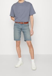 Blå bomulls t-shirt med kort ärm, matchad med ljusblå denimshorts. Brun läderbälte. Vita sneakers och strumpor till anklarna.