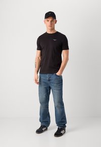 Tricou din bumbac negru cu decolteu rotund, blugi din denim albastru și adidași negri cu dungi albe; accesorizat cu o șapcă neagră.