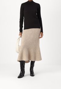 Maglione a collo alto nero a coste, gonna svasata beige texturizzata, stivali neri in pelle al ginocchio e borsa bianca. Outfit semplice e stratificato.