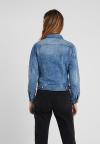 Světle modrá džínová bunda s přiléhavým střihem, zapínáním na knoflíky na manžetách a dvěma zadními kapsami. Vyznačuje se vybledlým vzhledem a klasickým límcem.