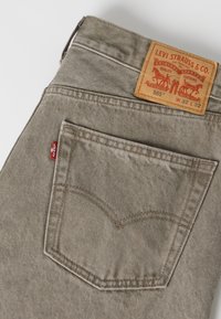 Πίσω τσέπη και ζώνη σε μπεζ τζιν Levi's με ορατή κόκκινη ετικέτα Levi's και δερμάτινη ετικέτα με την ένδειξη μεγέθους 32 x 32.