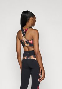 Fekete, rózsaszín díszítésű virágmintás sport crop top, magas derekú fekete leggings-szel párosítva, virágmintás derékrésszel.