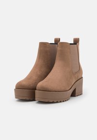 Hnědé z semišové ankle boots s elastickými postranními panely, masivní platformovou podrážkou a mírně zvýšeným podpatkem. Texturovaný svršek a hladký povrch.