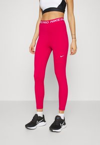 Dopasowane różowe legginsy sportowe z białym logo Nike i markowym pasem. Gładka tekstura i elastyczny materiał zapewniają komfort.