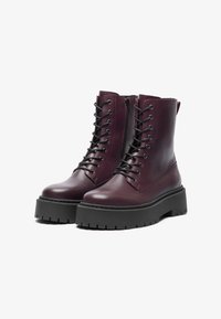Bottines en cuir bordeaux avec fermeture à lacets et fermeture éclair sur le côté, présentant une semelle noire épaisse et une plateforme texturée pour l'adhérence.