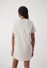 Vestido de manga corta color beige claro con un corte relajado y escote redondo, hecho de algodón suave. Presenta un diseño sencillo sin patrones.