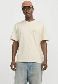 Beige katoenen T-shirt met korte mouwen en een losse pasvorm, voorzien van een klein "Originals Studio" logo in het groen op de linkerborst.