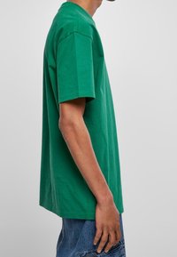 Zelené bavlněné tričko s volným střihem, krátkými rukávy a kulatým výstřihem. Hladká textura bez viditelných vzorů nebo akcentů.