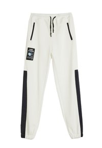Pantalones de chándal blancos con paneles laterales negros, cinturilla elástica, cordón y dos bolsillos con cremallera. Presenta una etiqueta "GAME CHANGER" en la parte frontal.