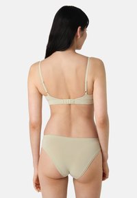 Completo di lingerie beige con un reggiseno semplice dotato di spalline regolabili e chiusura a gancio, abbinato a un perizoma in stile bikini. Texture liscia.