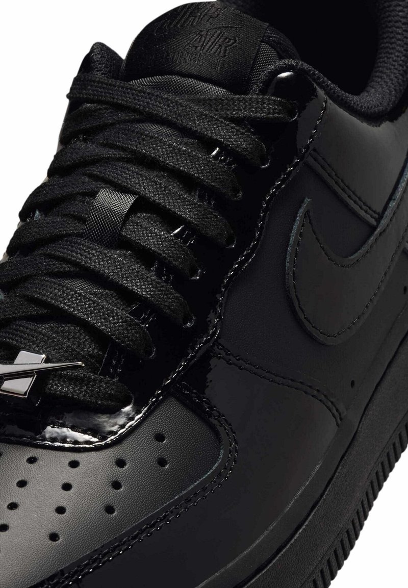 Primer plano de una zapatilla negra Nike Air Force 1 que muestra los cordones, el logo de Nike, perforaciones y suela texturizada.