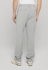 Pantalon gris clair, ajusté, avec une coupe décontractée, équipé d'une ceinture et de deux poches arrière ; associé à des baskets blanches et grises.