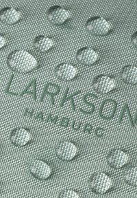 Tessuto verde chiaro con texture caratterizzato da un motivo di gocce d'acqua in rilievo e un marchio impresso, "LARKSON HAMBURG," in una tonalità di verde leggermente più scura.