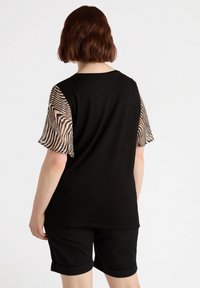 Maglietta nera con maniche corte in pizzo a fantasia animale; tessuto liscio; vestibilità comoda; abbinata a pantaloni corti neri arrotolati.