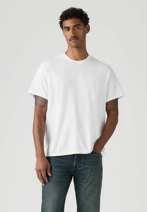 T-shirt bianca a maniche corte in cotone. Vestibilità comoda con collo tondo. Indossata con jeans denim blu dal look leggermente sbiadito.