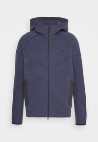 Marinblå Nike hoodie med dragkedja fram, ribbade ärmslut och två sidofickor. Har en åtsittande huva och diagonala sömmar som detalj.