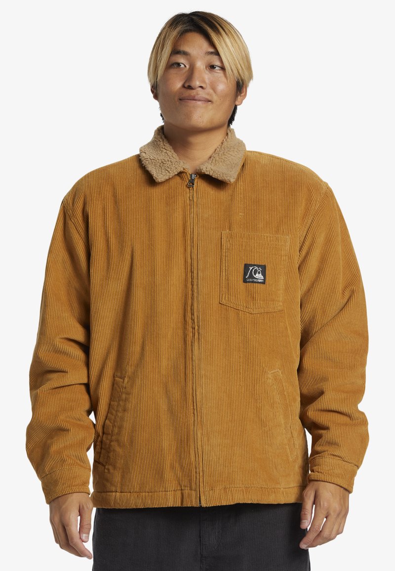 Fløjljakke i sennepsgul med en faux fur krave, lynlåslukning foran og brystlomme med en logo patch; ribbet tekstur gennem hele jakken.