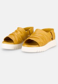 Gelbe Leder-Sandalen mit einem lässigen Design, das eine offene Zehenpartie, ein plissiertes Obermaterial und eine weiße Gummisohle mit strukturiertem Muster aufweist.